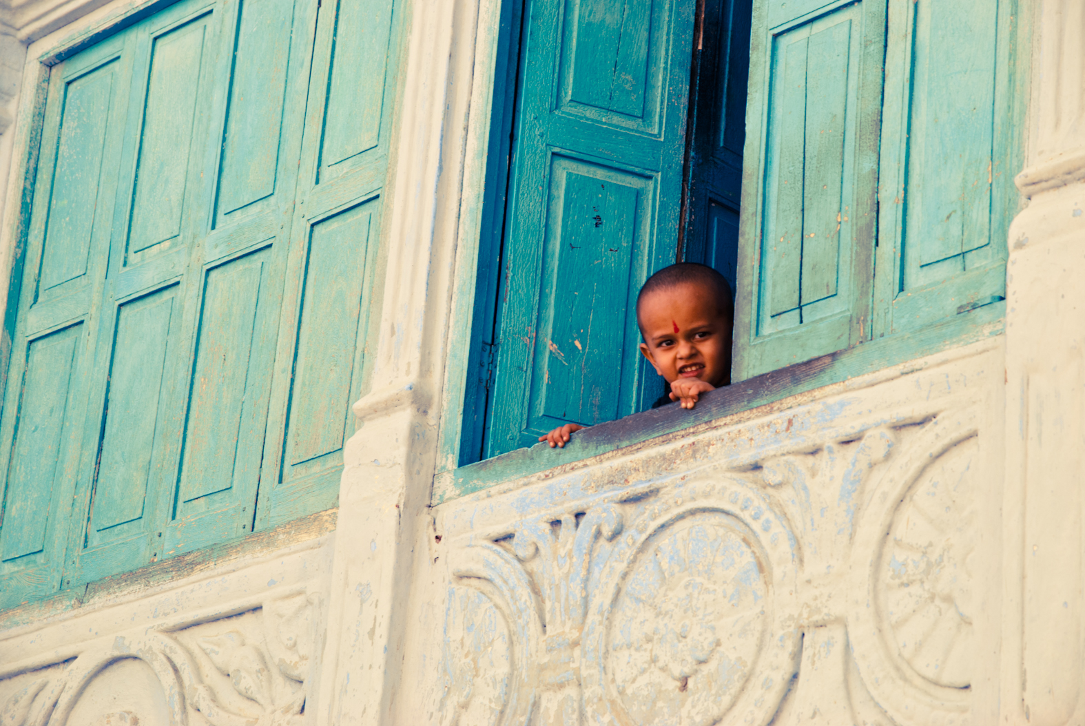 A child looking out between turquoise shutters