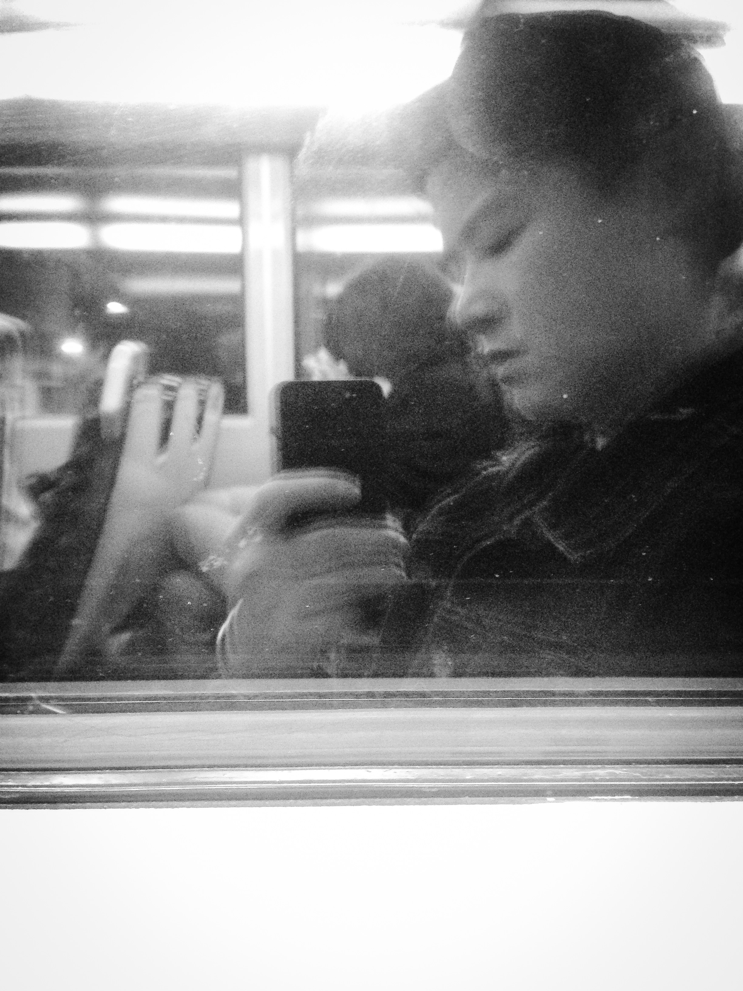 A face and a hand holding a phone, seen in a window